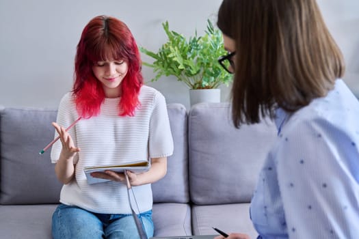 Teenage girl with notebook in hands at an individual lesson meeting with teacher mentor in office. Knowledge, education, teaching, tuition, high school adolescence concept