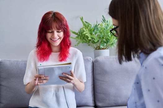 Teenage girl with notebook in hands at an individual lesson meeting with teacher mentor in office. Knowledge, education, teaching, tuition, high school adolescence concept