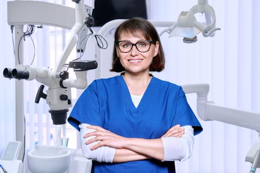 Portrait of smiling mature female dentist looking at camera in office. Positive middle aged doctor with glasses. Dentistry, medicine, health care, profession, treatment, stomatology concept