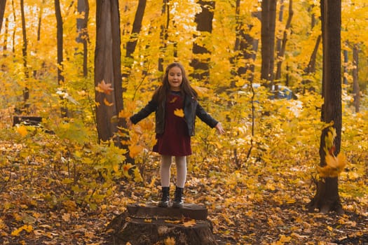 Little girl kid throwing autumn leaves on nature background - fall season and children leisure