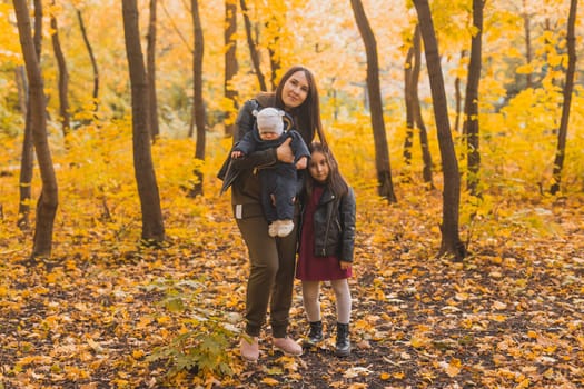 Caucasian mother with glasses is playing in leaves with her son and daughter during a walk in park