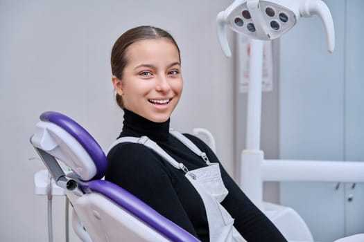 Portrait of young smiling teenage girl in dental chair looking at camera. Teenage female patient in dentist office. Adolescence, hygiene, treatment, dental health care