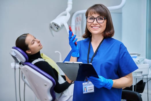 Smiling female dentist, nurse doctor with clipboard phone looking at camera in dental office. Dentistry, hygiene, treatment, medicine, dental health care concept