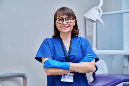 Portrait of female doctor dentist in office. Confident middle aged woman looking at camera with crossed arms near dental chair. Dentistry, medicine, specialist, career, dental health care concept