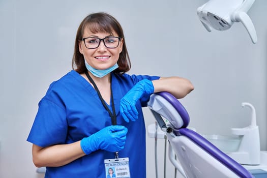 Portrait of smiling female doctor dentist in office. Confident middle aged woman looking at camera near dental chair. Dentistry, medicine, specialist, career, dental health care concept