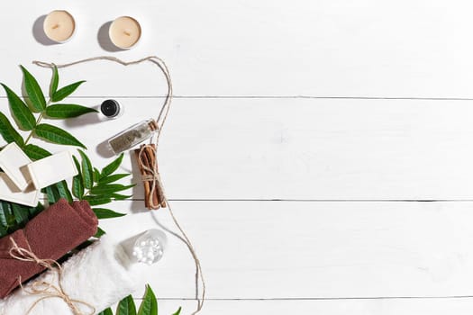 Natural handmade soaps with oil, cinnamon, candles, brown towel and green leaves on white wooden background. Top view. Copy space. Still life. Flat lay. SPA set