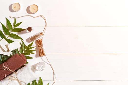 Natural handmade soaps with oil, cinnamon, candles, brown towel and green leaves on white wooden background. Top view. Copy space. Still life. Flat lay. SPA set. Sun flare