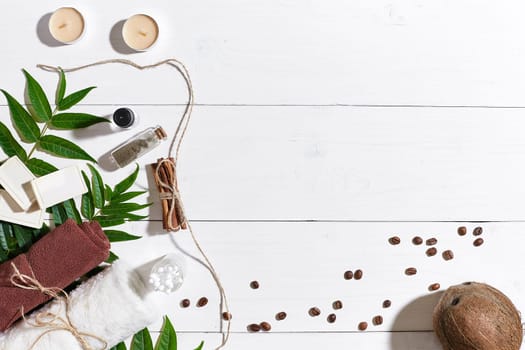 Natural handmade soaps with coffee beans, cinnamon, candles, oil, brown towel, coconut and green leaves on white wooden background. Top view. Copy space. Still life. Flat lay. SPA set
