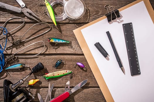 Accessories for fishing on the background of wood. Reel, fishing line, float, net hooks, lures for fishing. Top view. Still life. Copy space