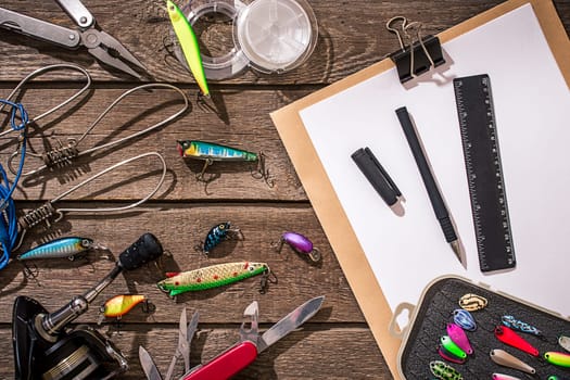 Accessories for fishing on the background of wood. Reel, fishing line, float, net hooks, lures for fishing. Top view. Still life. Copy space