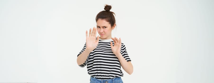 Image of woman refusing something, raising hands in defensive gesture, protecting herself, rejecting offer, declining, standing over white background.