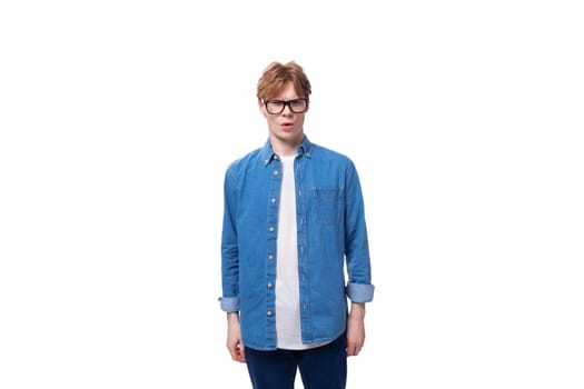 young smart red-haired guy dressed in a blue shirt wears glasses on a white background with copy space.