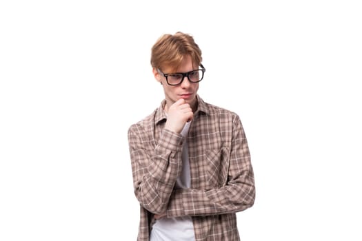 close-up portrait of a young dreaming caucasian man with red short hair in glasses and a shirt on a white background.