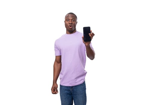 young smart african man dressed in a lilac t-shirt and jeans uses a smartphone.