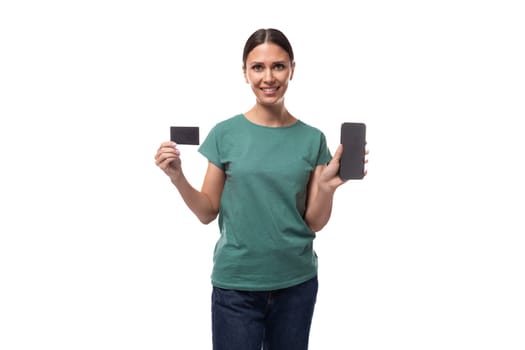 young energetic slender european woman with a ponytail hairstyle is dressed in a green t-shirt holding a smartphone and a credit card.