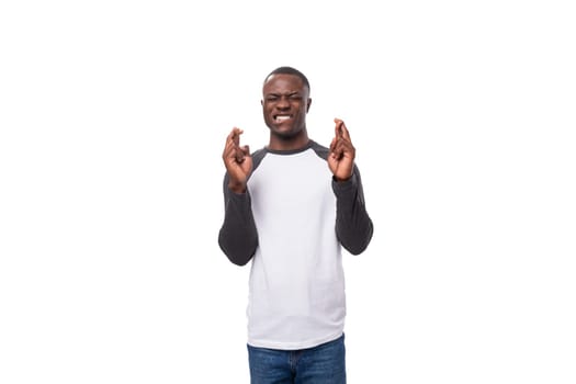 young positive african man dressed in a spring jacket crossed his fingers and hopes for the best.