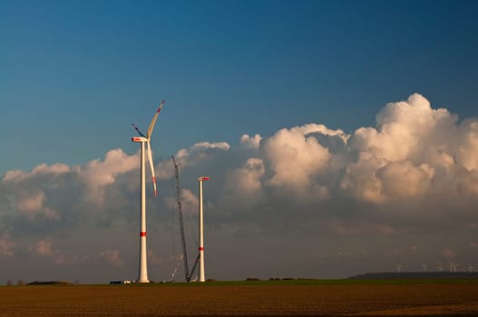 Wind turbines under construction,with coal-fired power plant in the background against blue sky