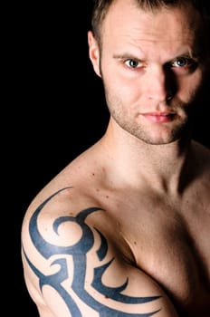 Young man showing his tribal tattoo on his shoulder, isolatad against black background.