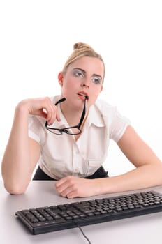 Young woman with blond hair wearing a business suit and has bored in the office. You sitting bored in front of the keyboard and chews on her glasses, isolated against white background.