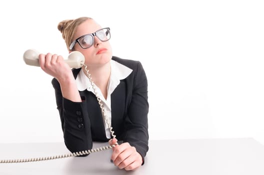 Young woman with blond hair wearing a business suit and has frustrated the computer. She sits at her keyboard and looks annoyed at the camera, isolated against white background.