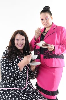 About two faithfully models wear flashy costumes and chat over coffee and cake, isolated against white background.