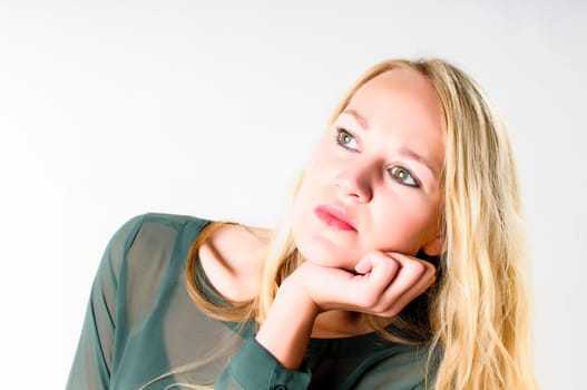 Attractive young woman with long blond hair has her chin resting in her hand and is looking pensively into the air,isolated against a white background.