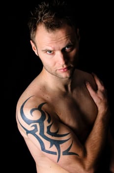 Young man showing his tribal tattoo on his shoulder, isolatad against black background.
