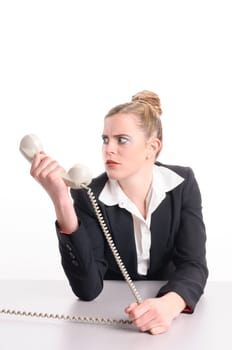 Young woman with blond hair wearing a business suit and has frustrated the computer. She sits at her keyboard and looks annoyed at the camera, isolated against white background.