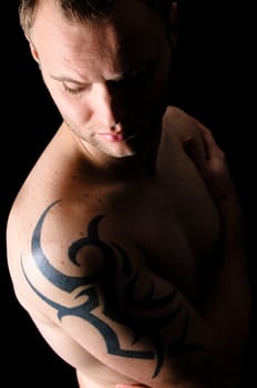 Young man showing his tribal tattoo on his shoulder, isolatad against black background.