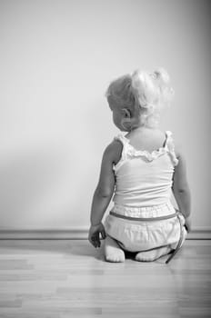 little girl sits on her knees facing the wall