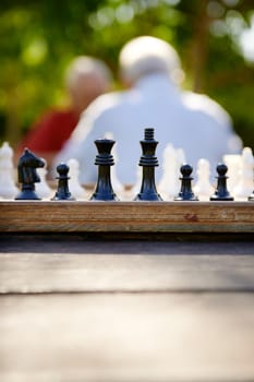 Active retirement, old friends and leisure, two senior men having fun and playing chess game at park. Focus on chessboard in foreground