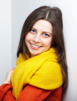 Portrait of a beautiful young woman with yellow scarf leaning against a white wall.