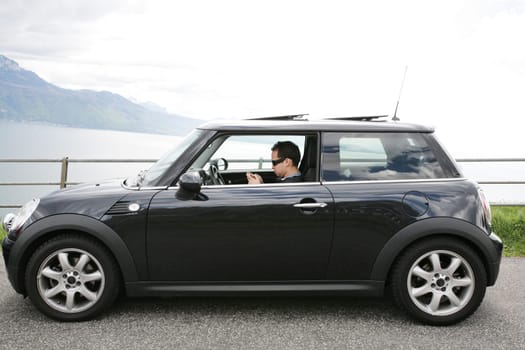 Young man in his fancy car chatting with his device up the hills