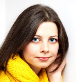 Portrait of a beautiful young woman with yellow scarf leaning against a white wall.