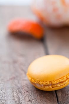 Closeup of yellow macaroon resting on wooden table with peeled orange in background