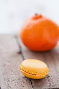 Closeup of yellow macaroon resting on wooden table with orange in background