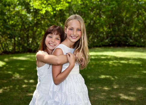 Outdoor photo of two young girls wearing white dresses with green foliage background