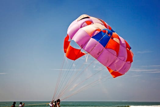 Landscape of paraglider taking off with the parachute leaving a trail of sand blowing in the breeze watched by roadies and friend, location of shot GUttorda Beach, Goa, India, colorful generic, holiday, destination