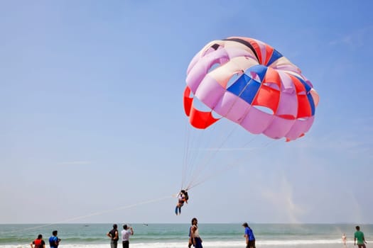 Landscape of paraglider taking off leaving a trail of sand blowing in the breeze watched by friends and public at Uttorda Beach in Goa India a popular holiday destination