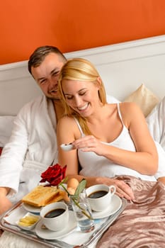 Happy lovers lying bed eating romantic breakfast together morning