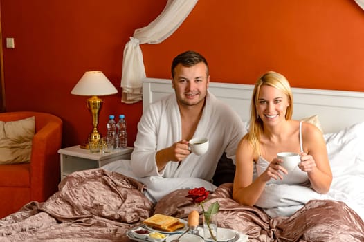 Sitting happy husband wife bed drinking tea romantic hotel breakfast