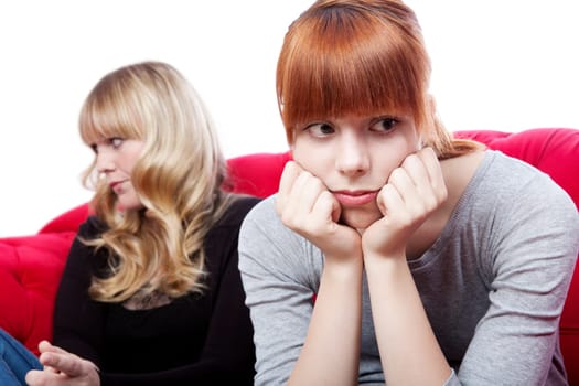 young beautiful blond and red haired girls sitting on red sofa and are sad and depressed in front of white background