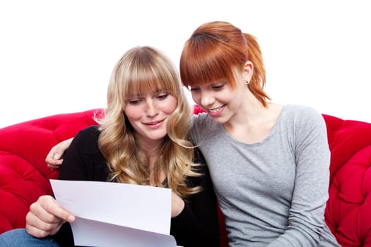 young beautiful blond and red haired girls on red sofa reading letter in front of white background