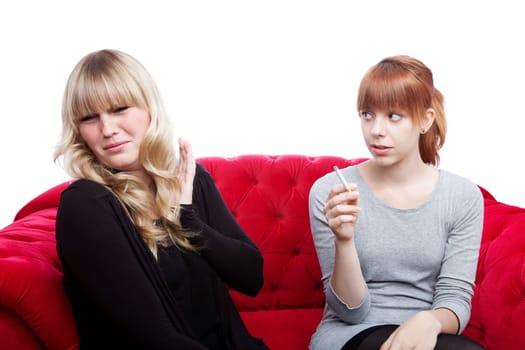young beautiful blond and red haired girls is disgusting becuase of smoker on red sofa in front of white background