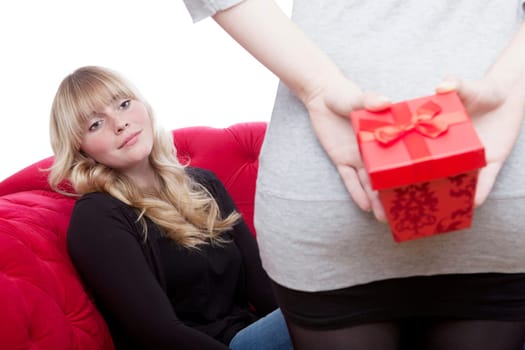 young beautiful blond and red haired girls on red sofa have a present box in front of white background