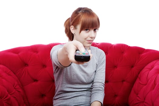 young beautiful red haired girl changing channel on red sofa in front of white background