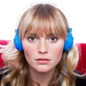 stunning young blond haired girl with headphones on red sofa in front of white background
