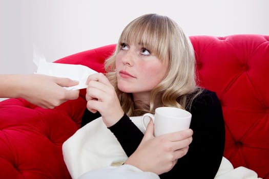 young beautiful blond and red haired girls has a cold and get a hankie on red sofa in front of grey background