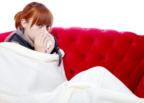 young beautiful red haired girl on red sofa is sick in front of white background