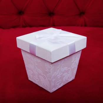 beautiful white gift box with ribbon on top of red sofa background